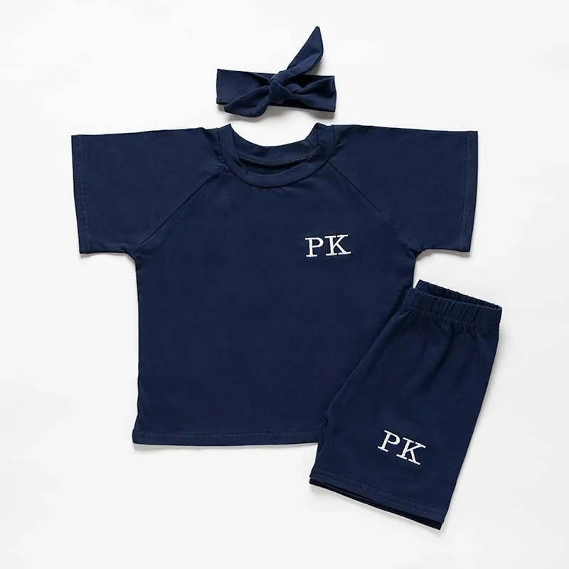 Navy baby top, shorts and hair bow laid flat on white