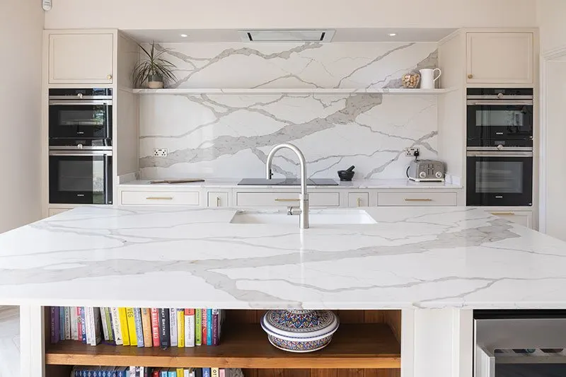 Bright marble kitchen with an island, tall ovens and a herringbone floor