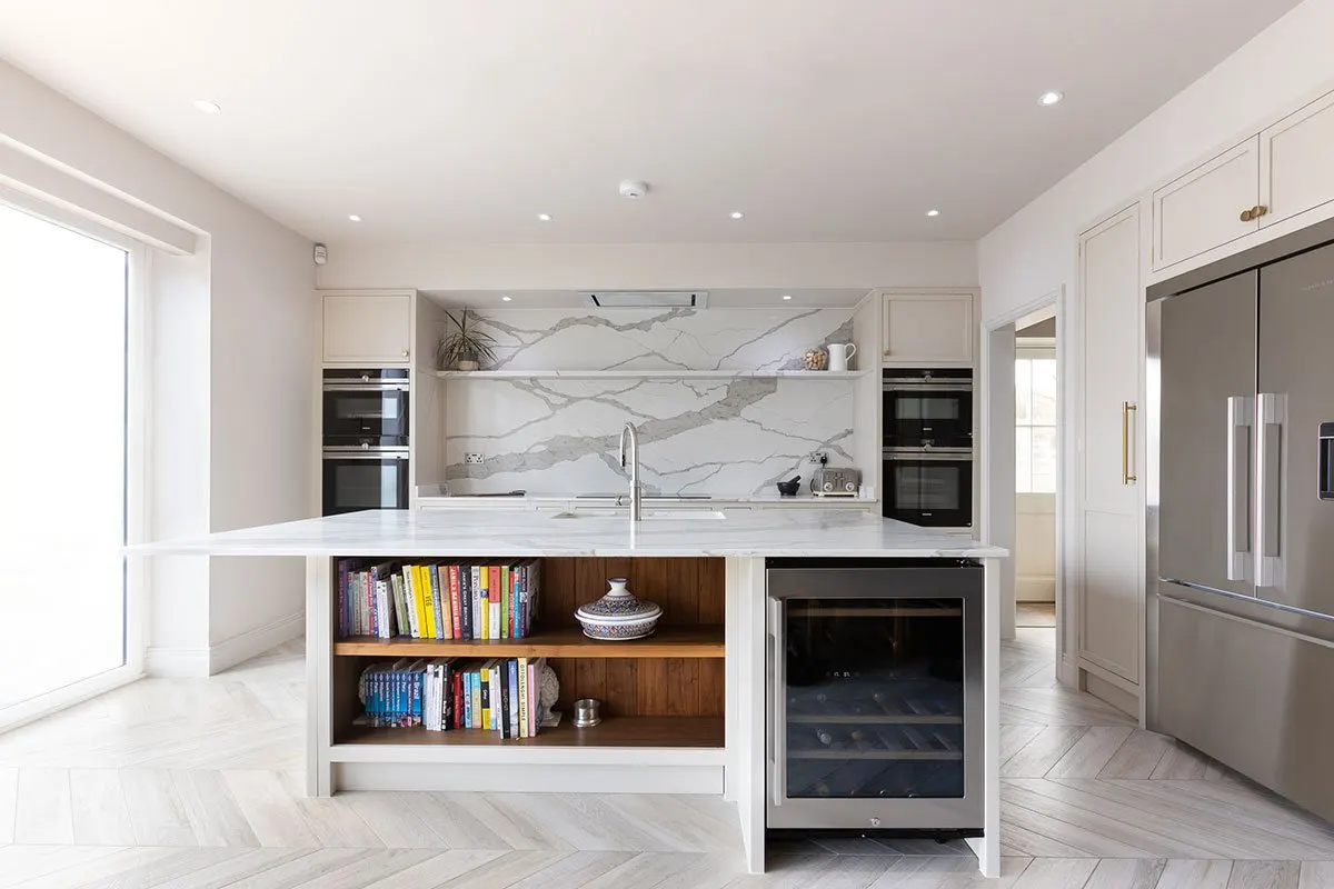 Marble kitchen island with bookshelves and a wine fridge, ovens behind
