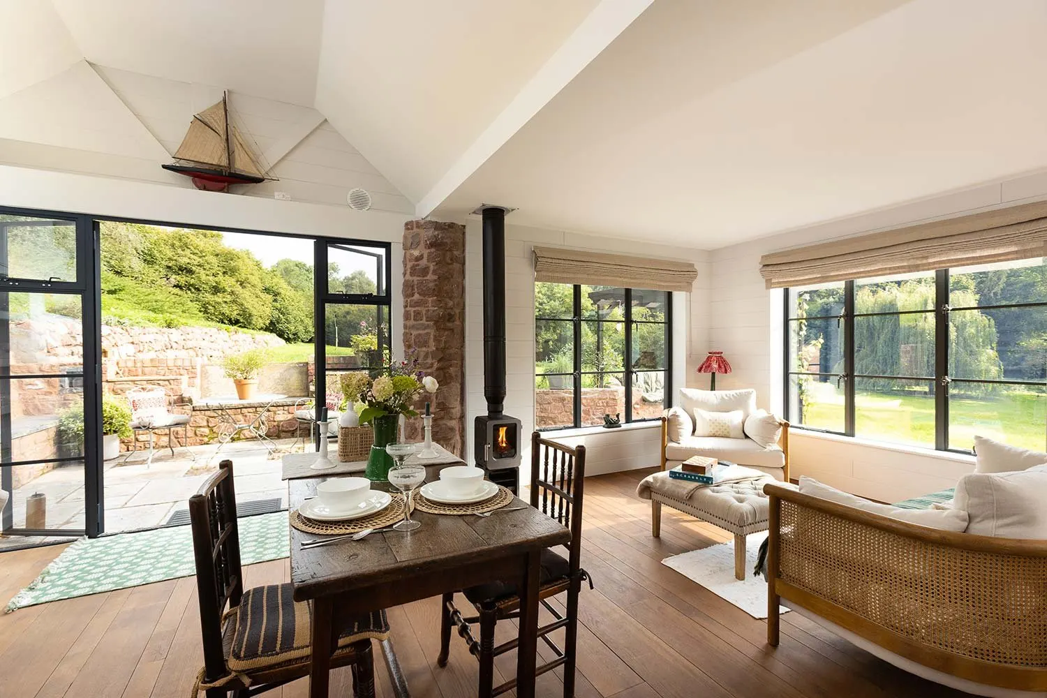 Open-plan cabin interior with a wood-burning stove and doors open to the garden